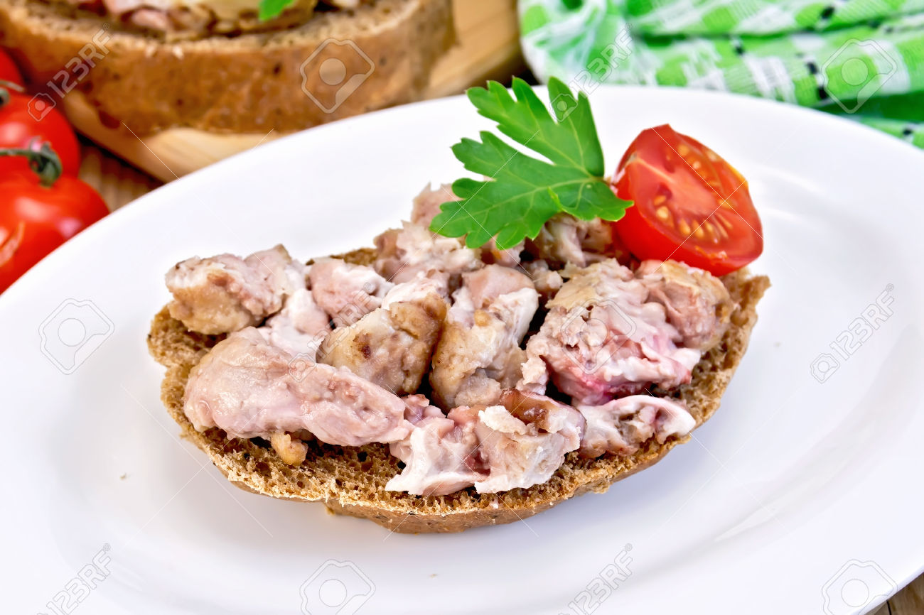 A sandwich of rye bread with brains, tomato and parsley on an oval plate on a wooden boards background